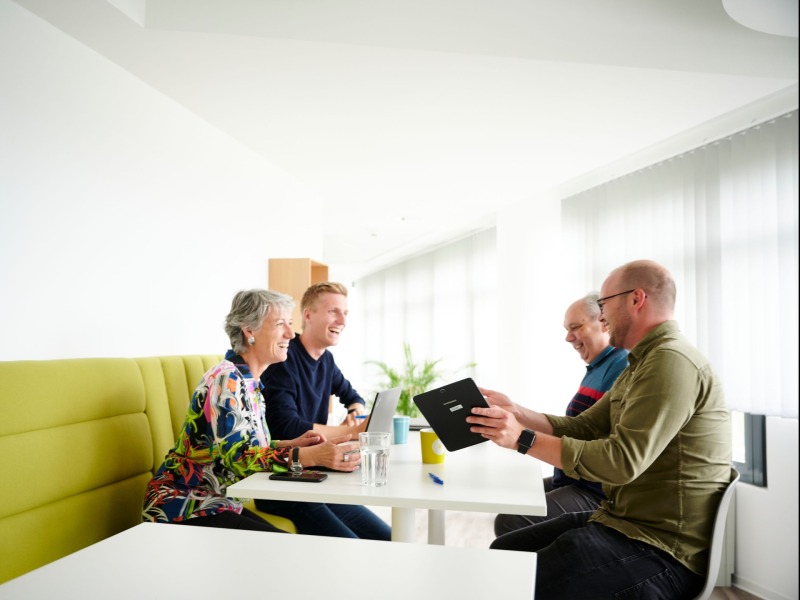 drei Männer und eine Frau sitzen an einem Hochtisch und sprechen über eine Präsentation